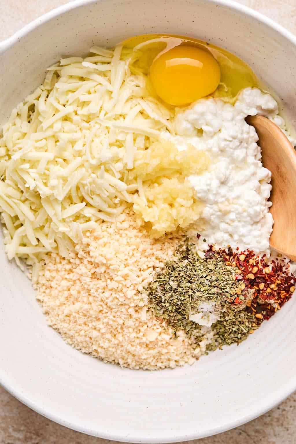 Cottage cheese, parmesan egg and other ingredients in mixing bowl with wooden spoon.