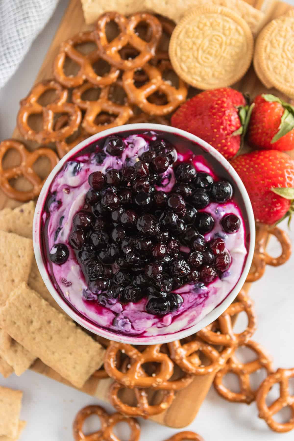 Blueberry cheesecake dip on platter with graham crackers, strawberries, pretzels.