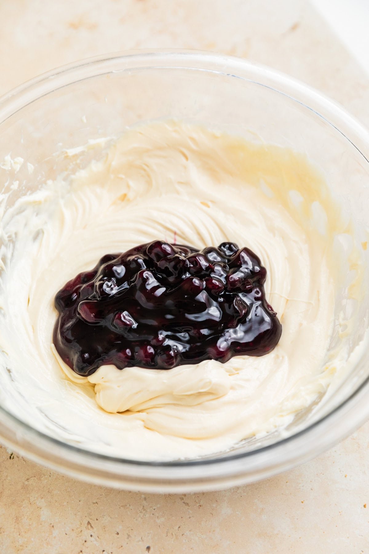 Blueberry pie filling added to cheesecake dip mixture in glass bowl.