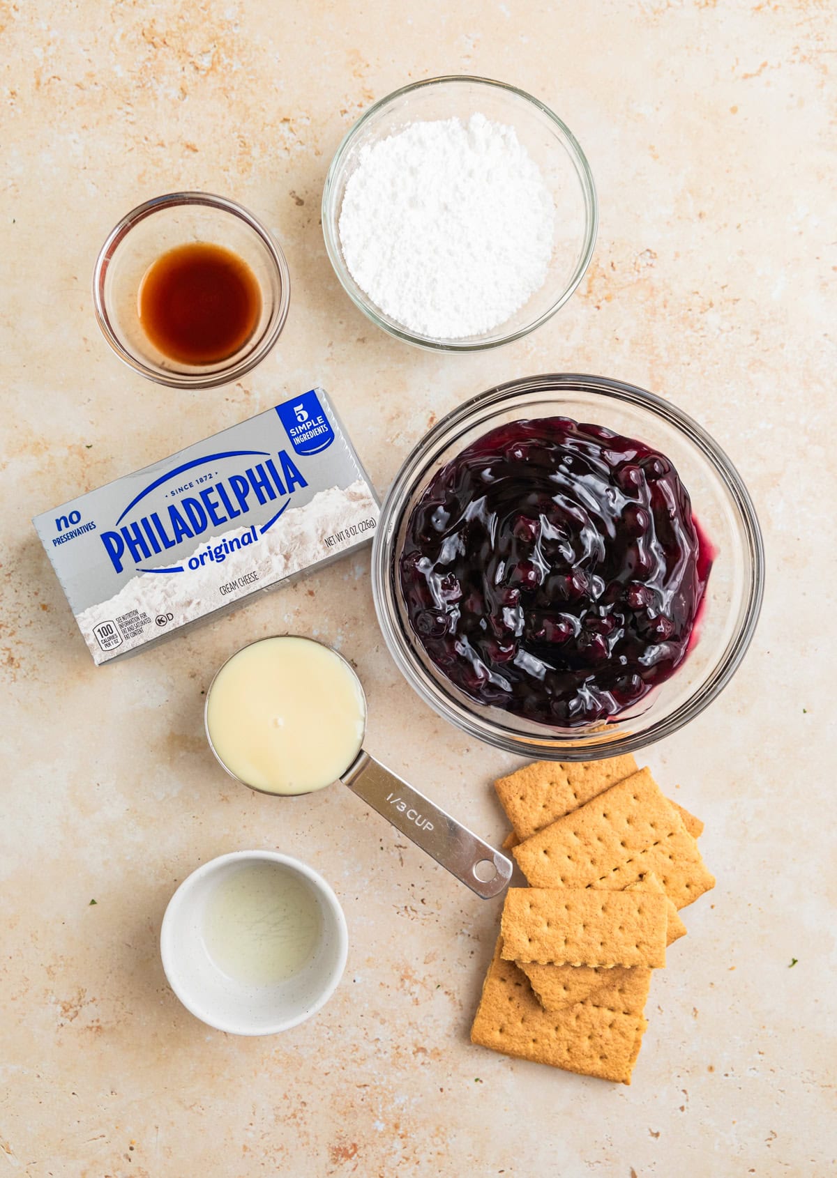 Cream cheese, blueberry pie filling and other ingredients arranged on surface.