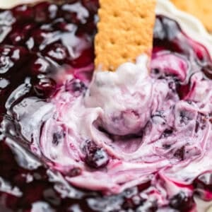 Graham cracker dipped into cheesecake dip topped with blueberries.