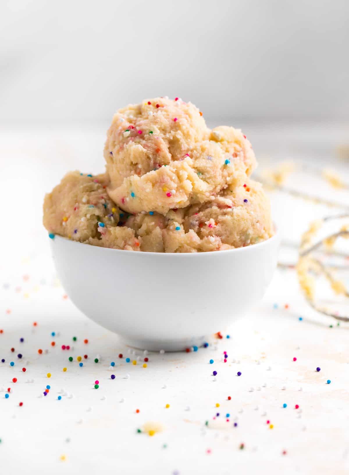 Bowl of sugar cookie dough scooped with funfetti sprinkles.