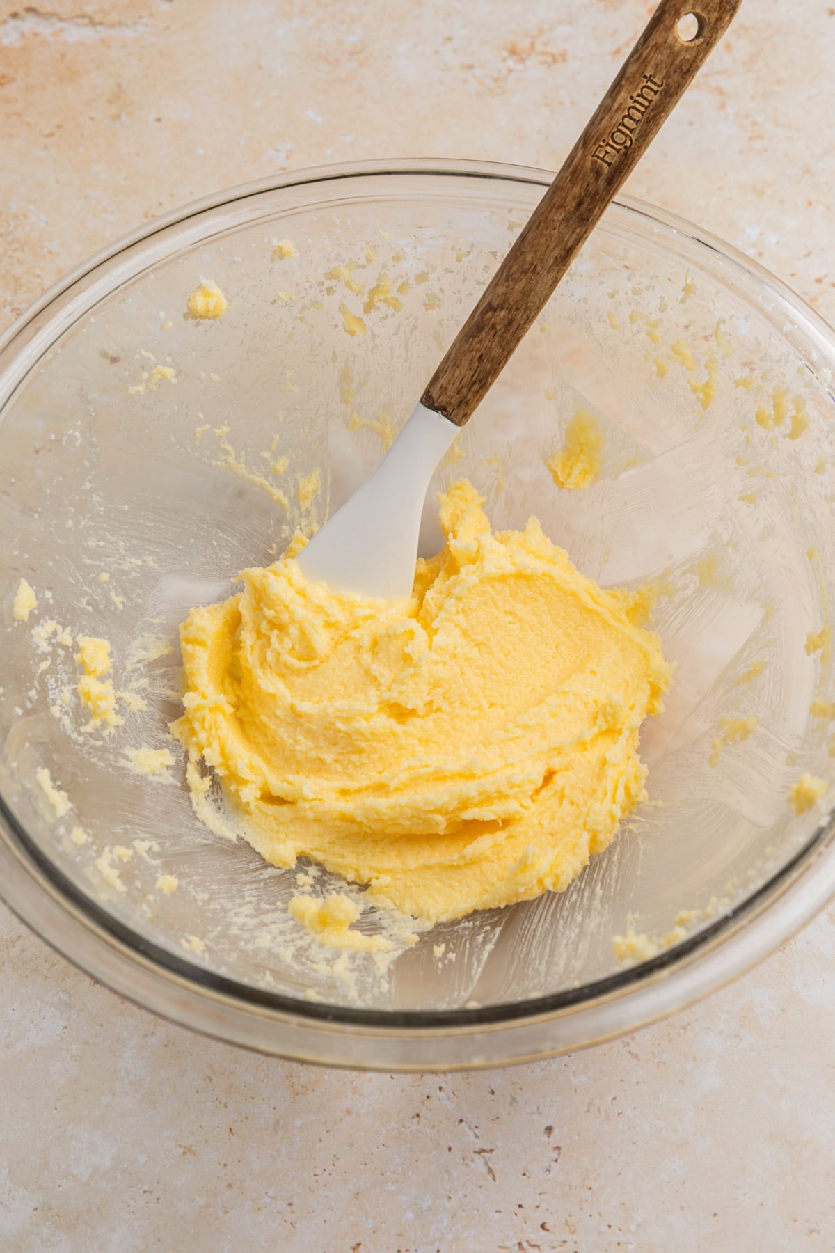 Creamed butter and sugar in glass mixing bowl with spatula.