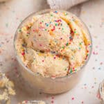Edible sugar cookie dough with sprinkles in cup topped with more sprinkles.