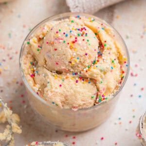 Edible sugar cookie dough with sprinkles in cup topped with more sprinkles.