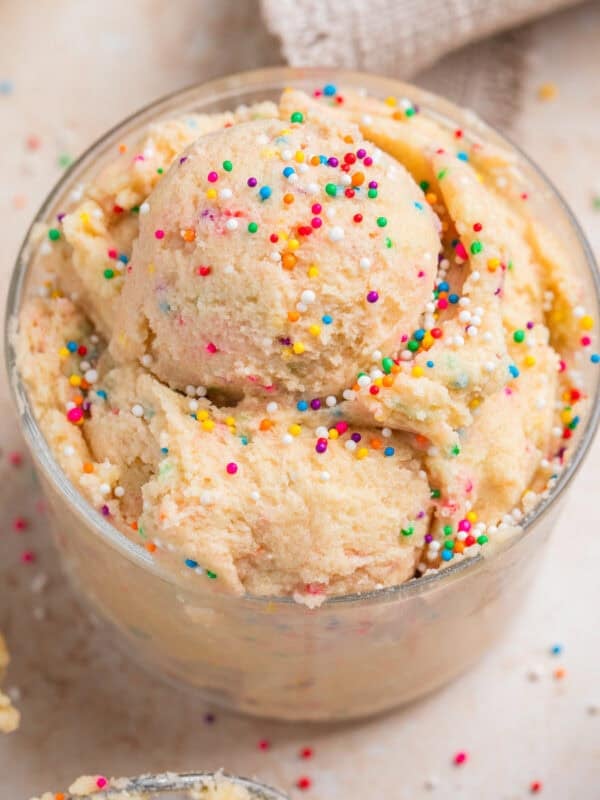Edible sugar cookie dough with sprinkles in cup topped with more sprinkles.