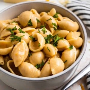Creamy macaroni and cheese shells in clay bowl with chopped fresh parsley on top.