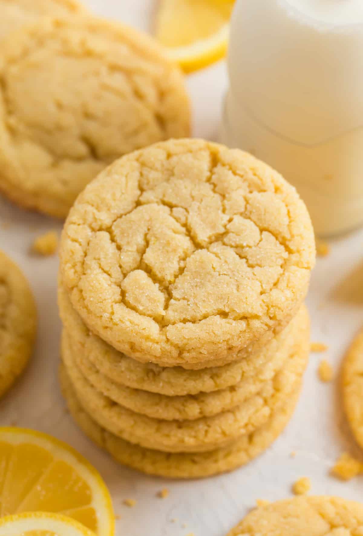 Stack of lemon sugar cookies with glass of milk and lemon wedges surrounding.