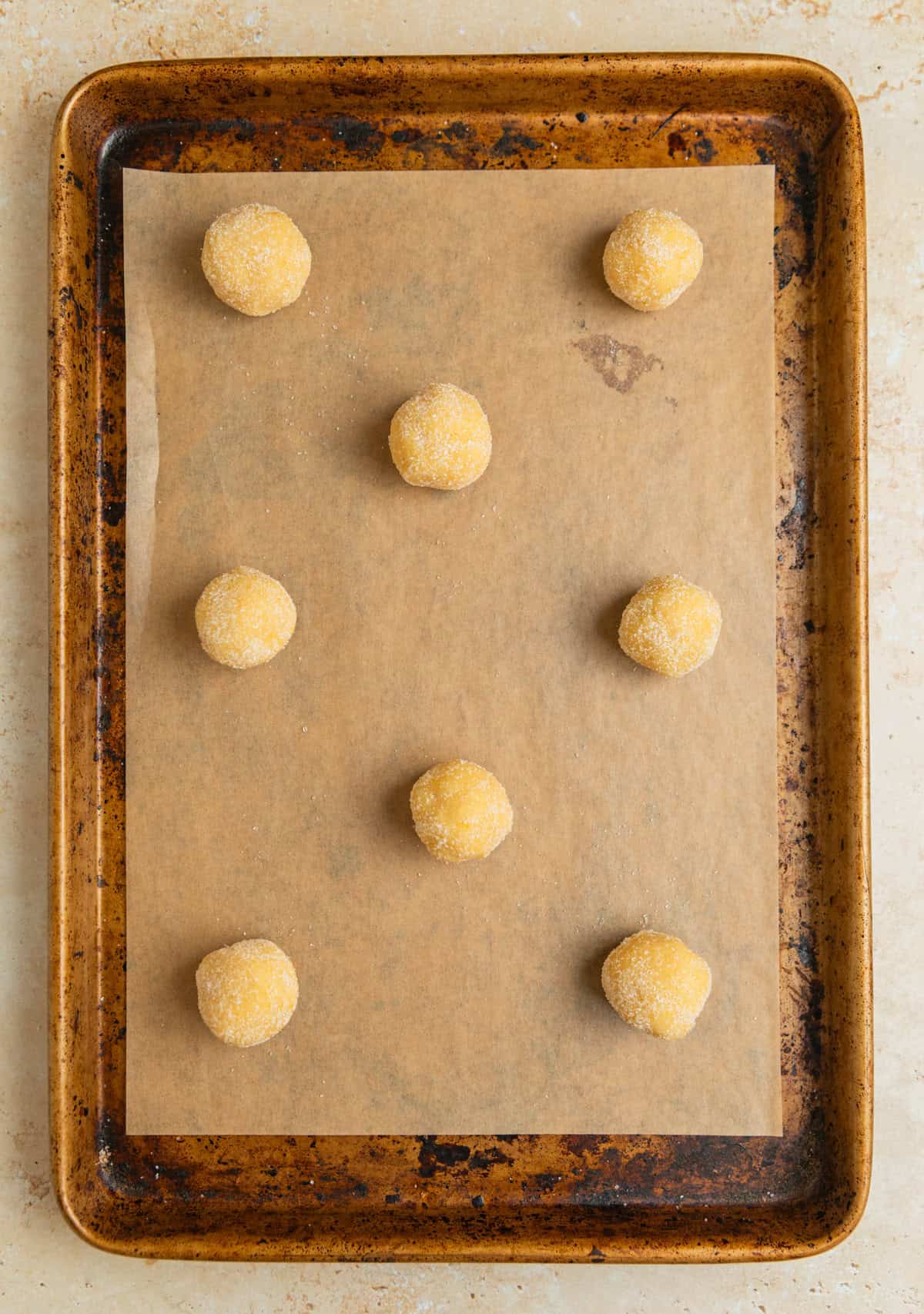 Rolled cookie dough balls rolled in sugar on parchment lined cookie sheet.