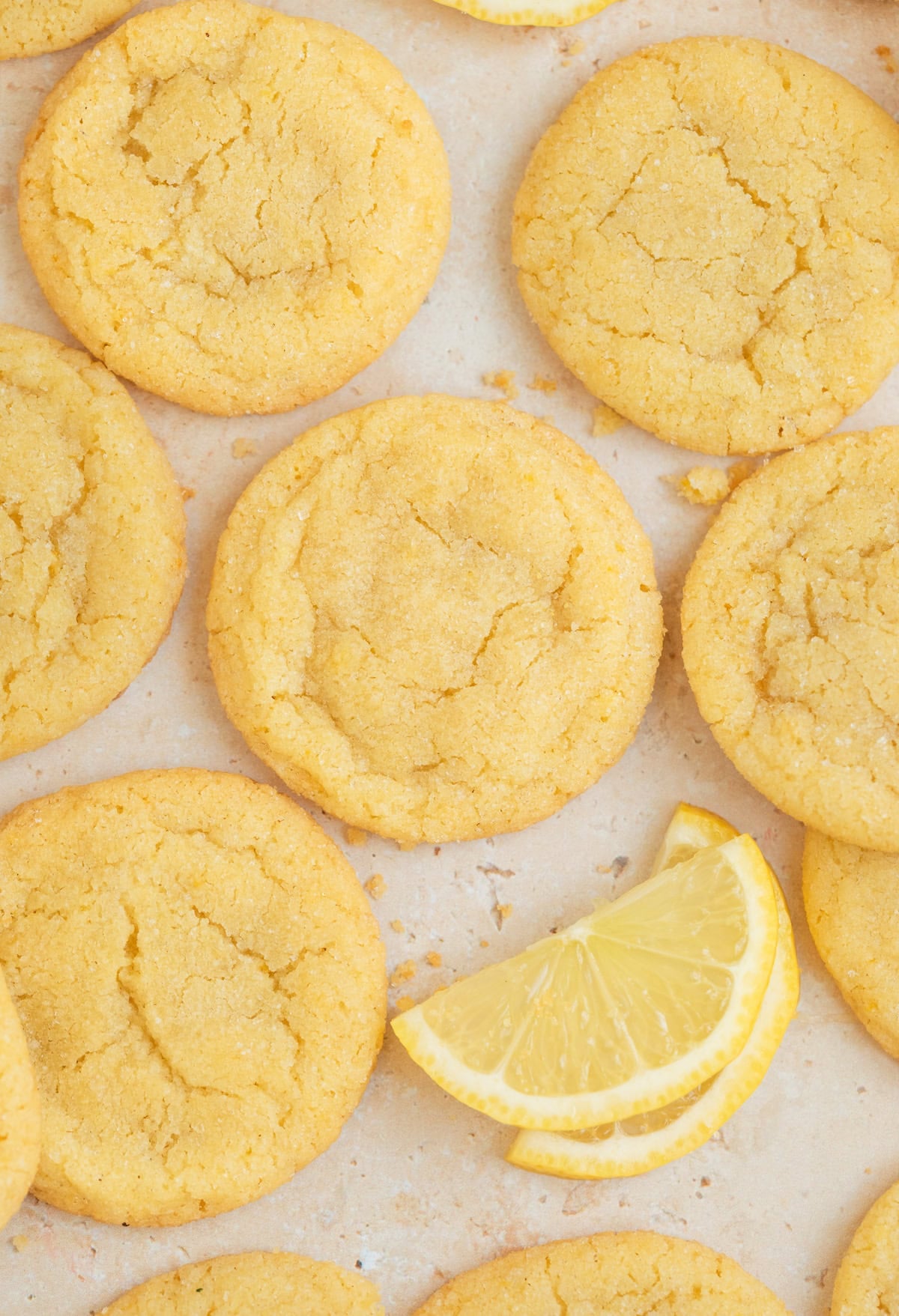 Lemon cookies on surface with lemon wedges and crumbs.