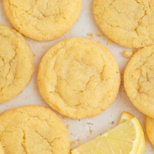 Lemon sugar cookies on surface with lemon wedges.