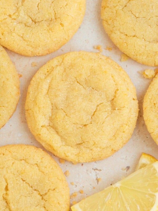 Lemon sugar cookies on surface with lemon wedges.