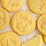 Lemon sugar cookies on surface with lemon wedges.