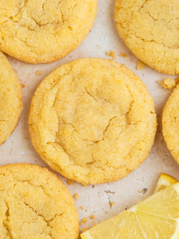 Lemon sugar cookies on surface with lemon wedges.