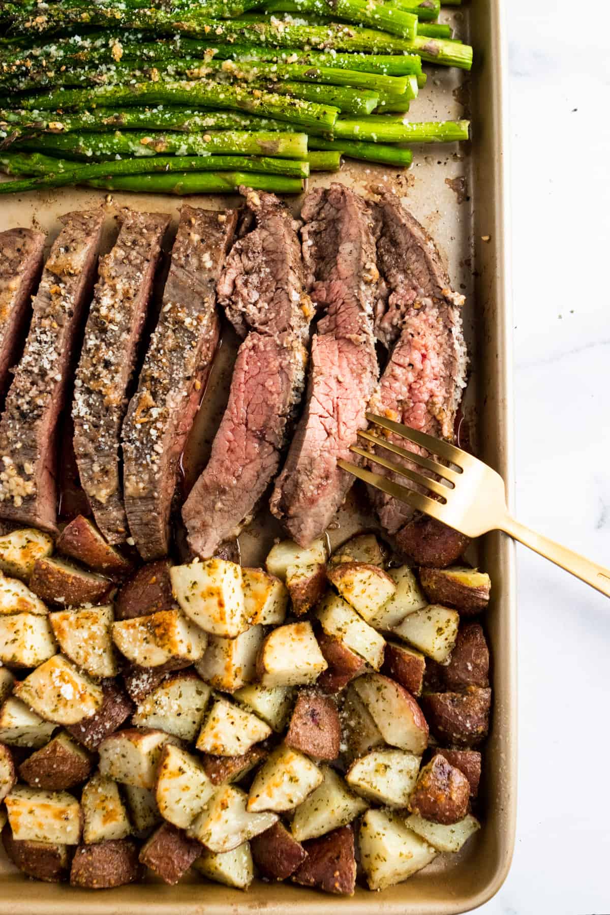 Parmesan crusted steak with potatoes and asparagus on sheet pan.