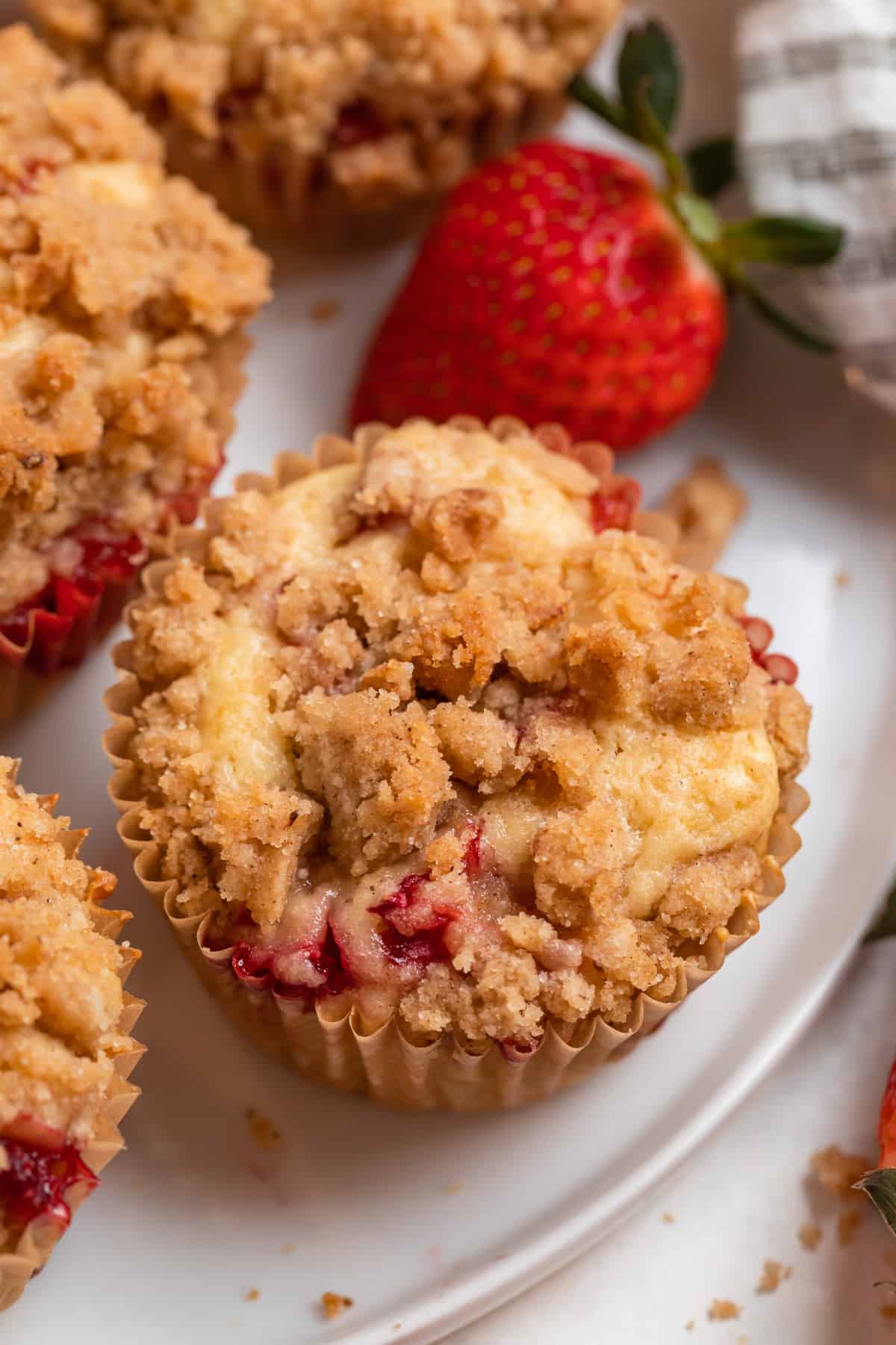 Strawberry crumb muffins on white plate with strawberries beside.
