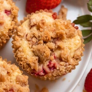 Strawberry crumble muffins on white plate with berries.