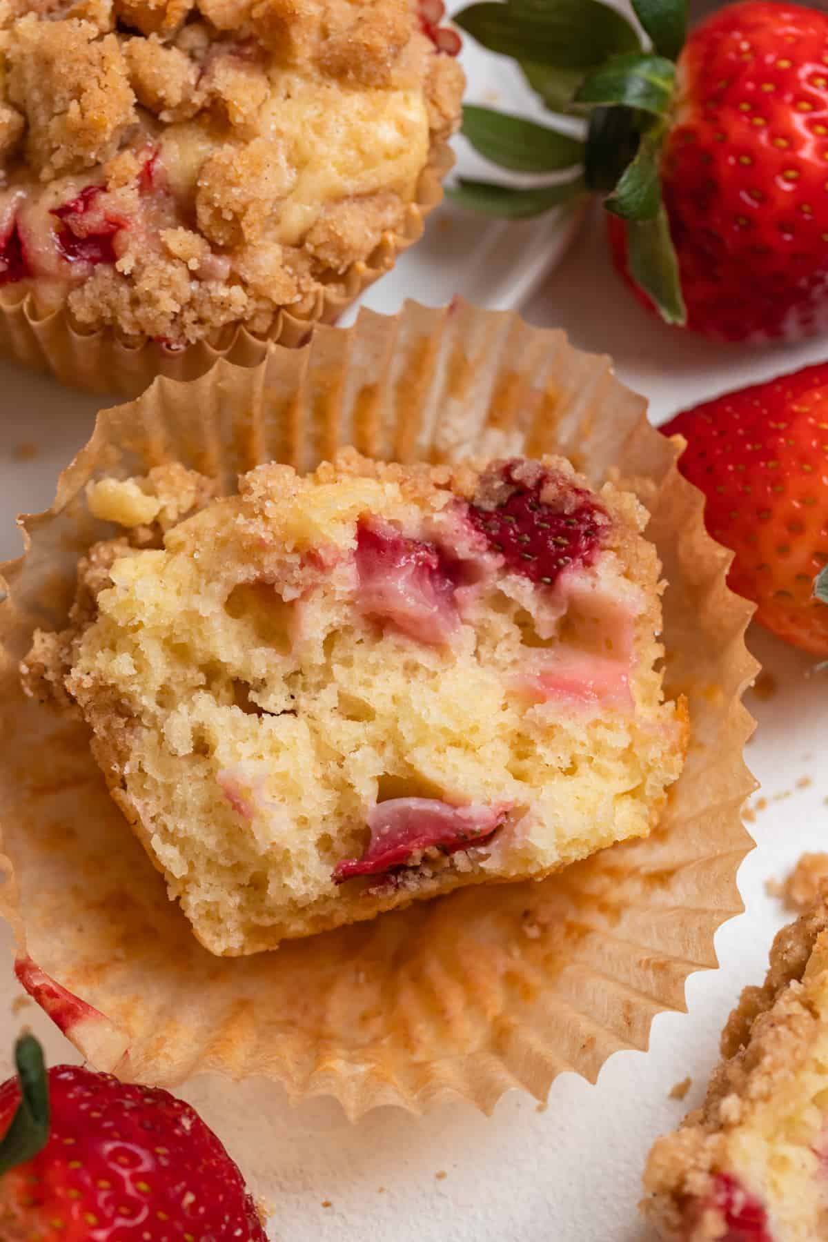 Halved strawberry crumb muffin on muffin cup with berries around it.