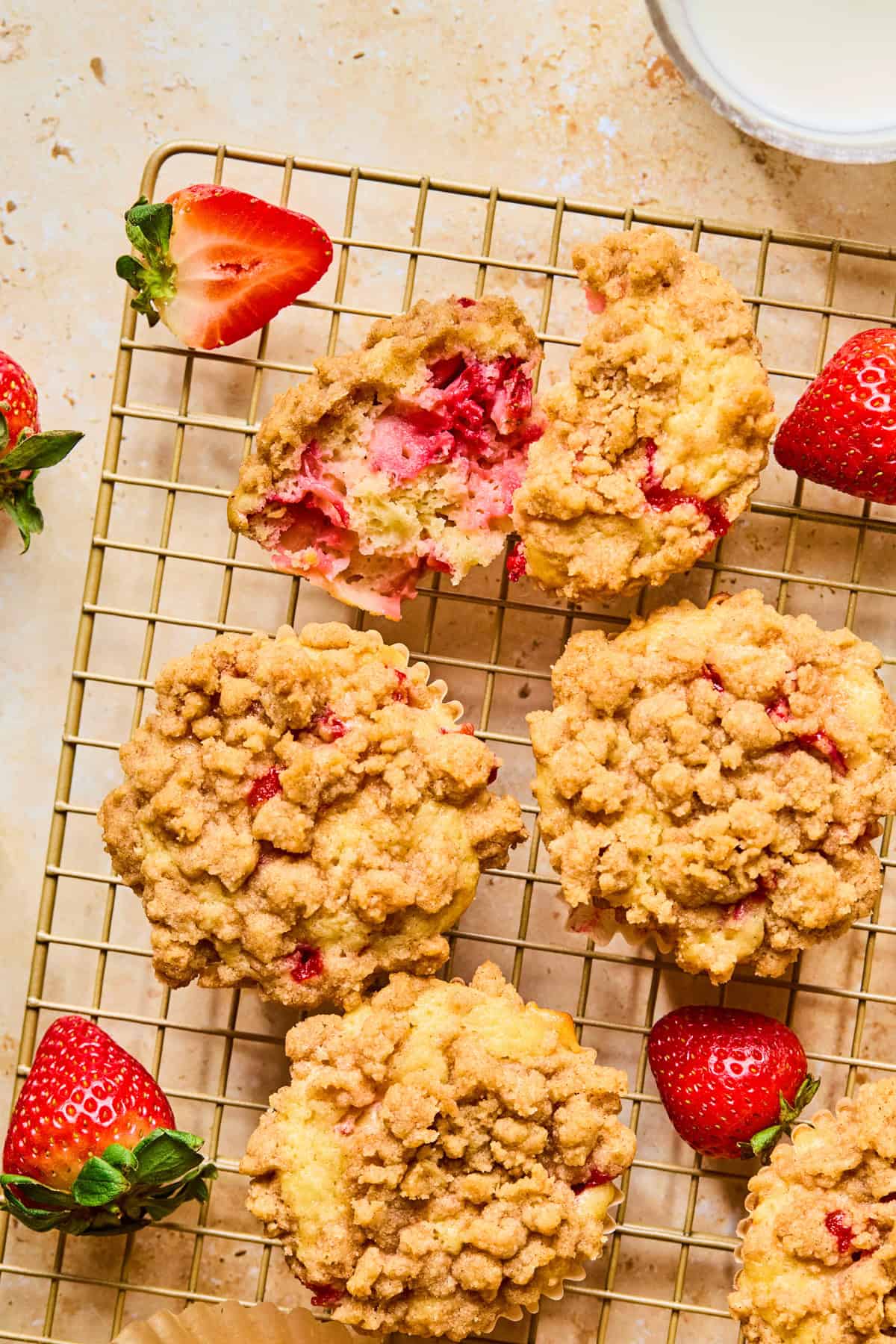 Halved strawberry crumb muffin on muffin cup with berries and muffins around it.