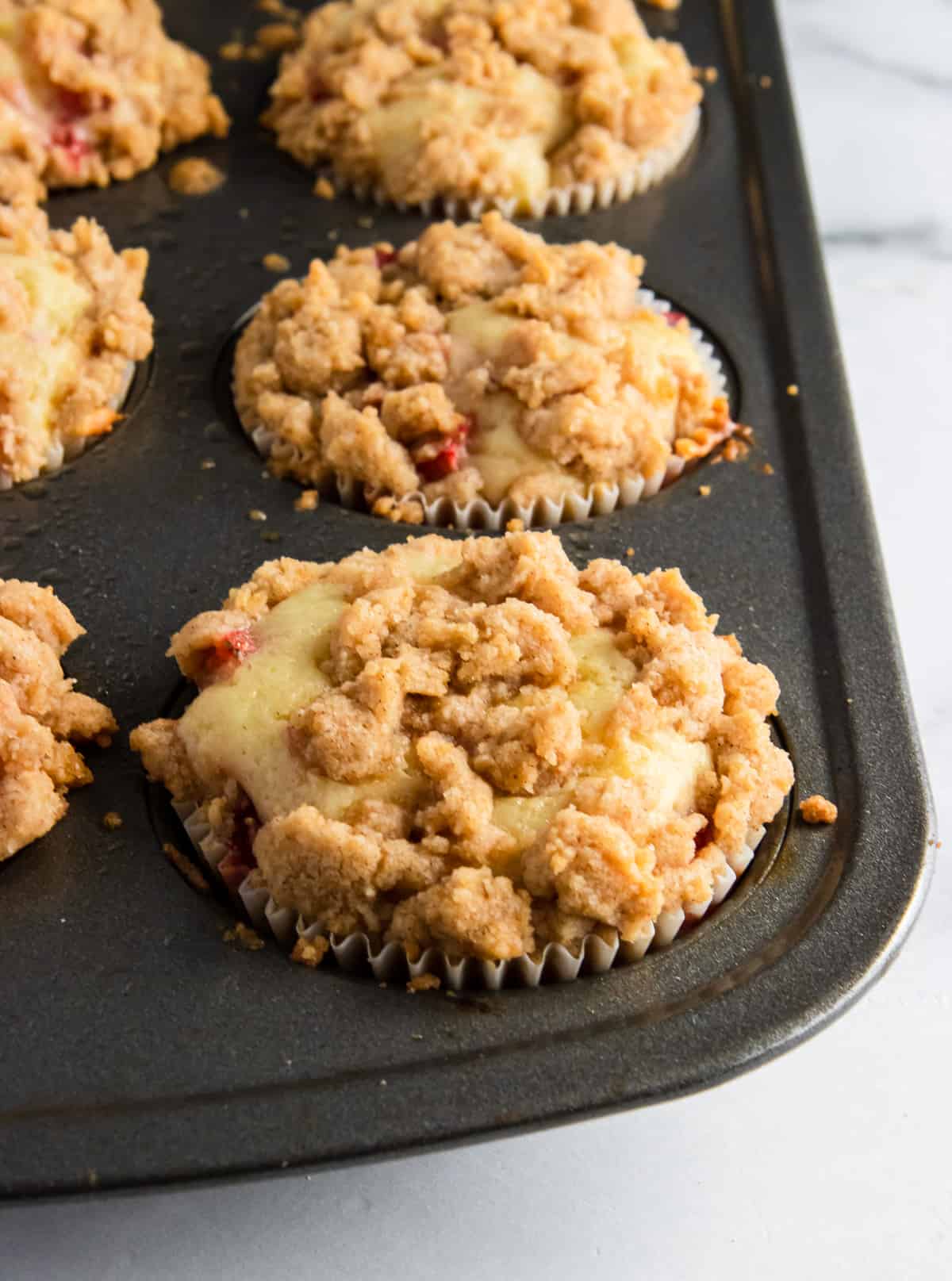 Freshly baked strawberry muffins with crumble topping in muffin tin.