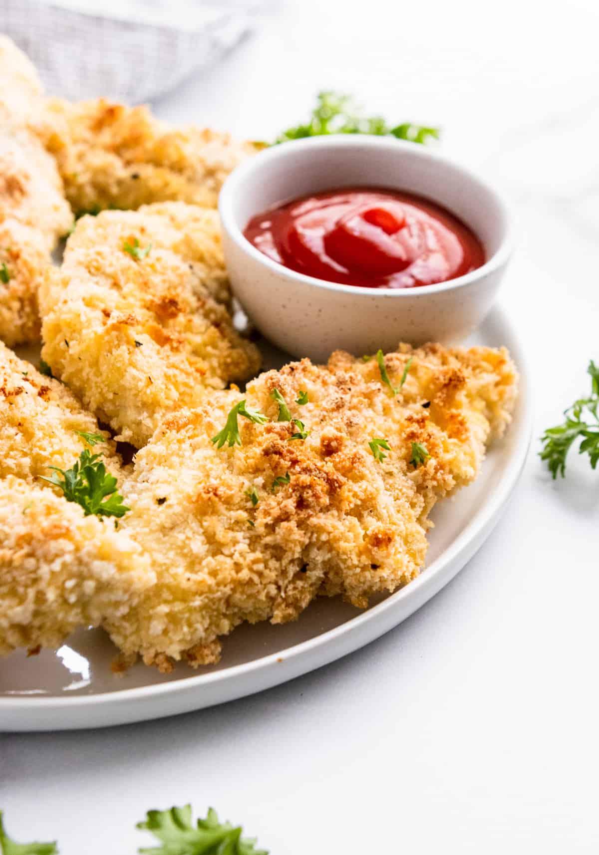 Cornmeal baked breaded chicken tenders on white plate with ketchup.