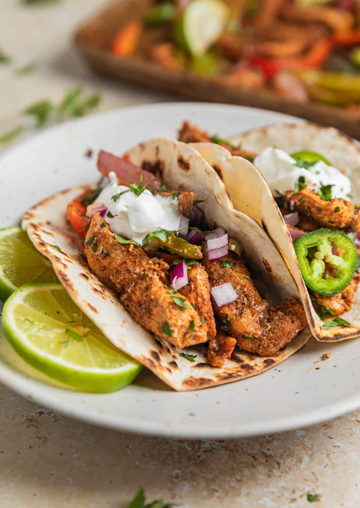 Honey lime chicken fajitas on tortillas on plate with sour cream dollop on top.