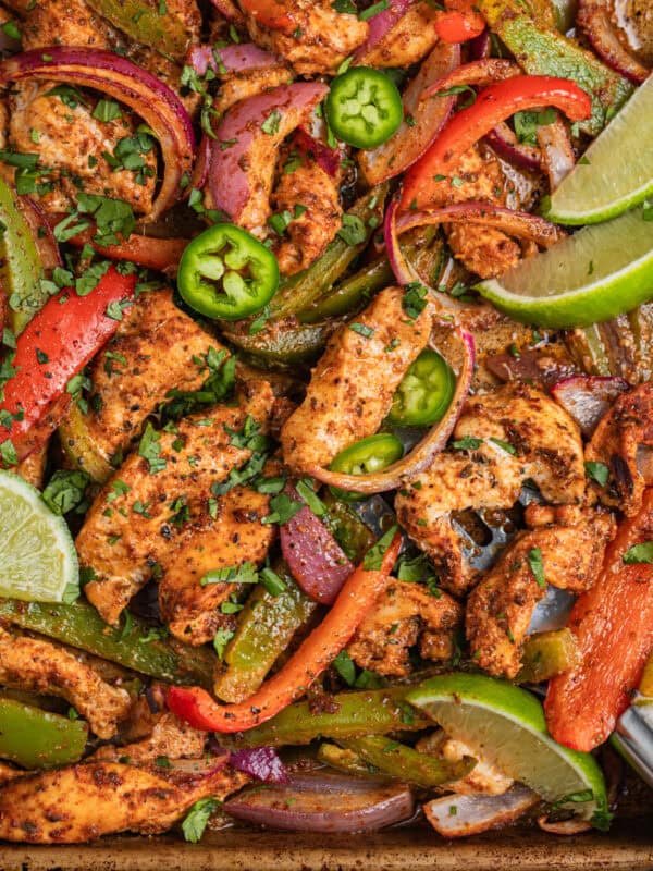 Baked chicken fajitas on sheet pan with spatula scooping onto the pan.