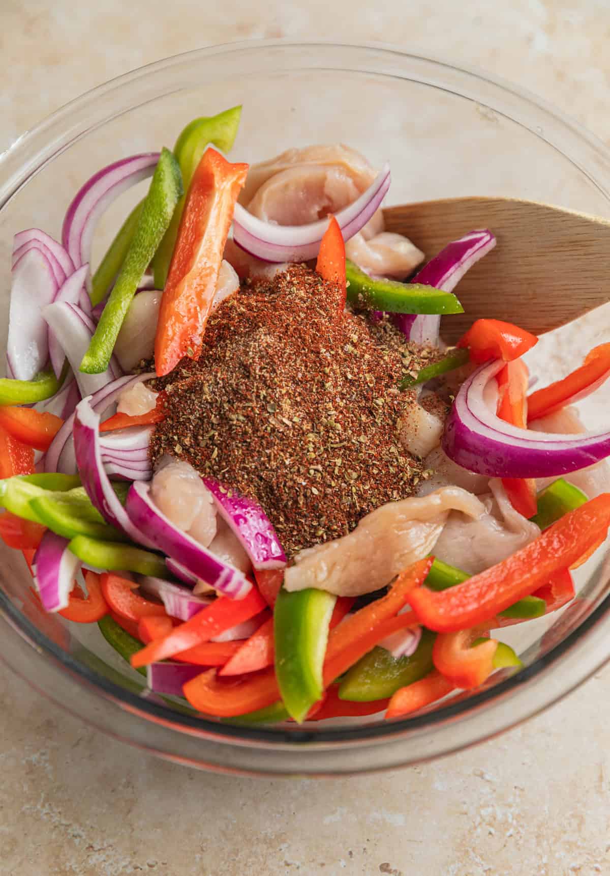 Fajita seasoning and marinade ingredients added to bowl with chicken and veggies.