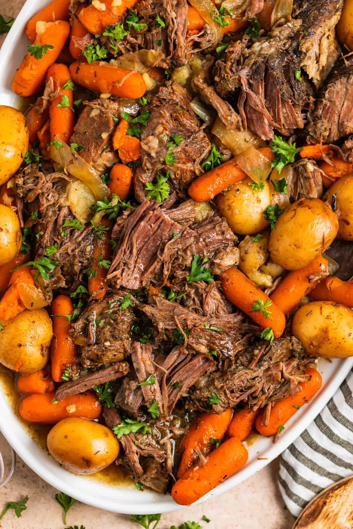 Overhead view of white platter with shredded chuck roast, carrots, potatoes and onion.