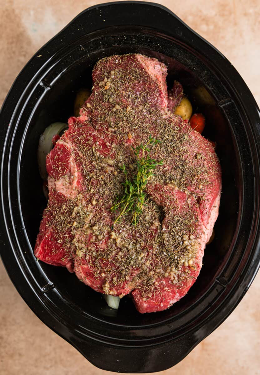 Seasoning and fresh thyme covering chuck roast in crock pot.