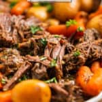 White serving platter with slow cooked roast beef chunks, carrots, potatoes and onion topped with parsley.