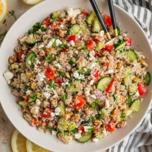 Cucumber quinoa salad in bowl with peppers, feta, chopped dill and serving utensils.