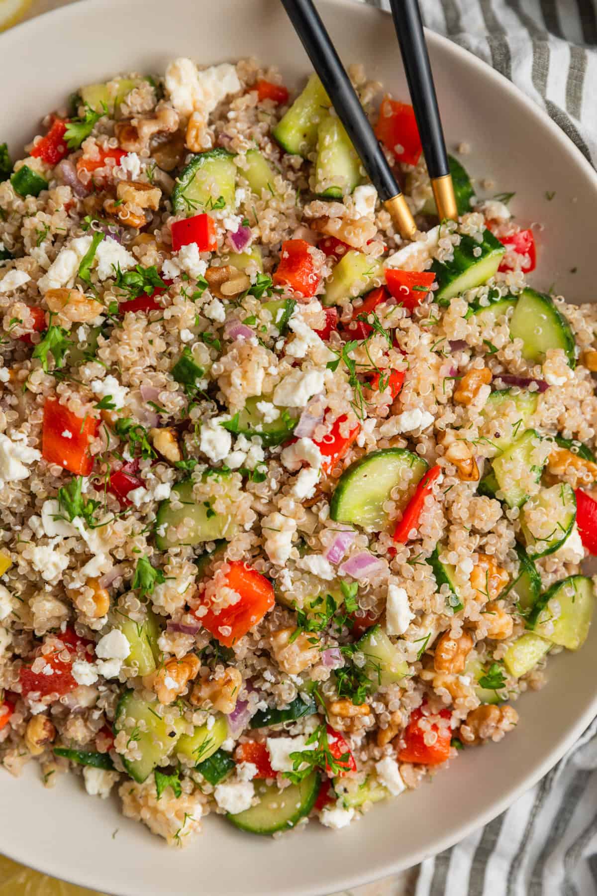 Large bowl with quinoa salad with cucumbers, feta cheese, red pepper, onion, and other ingredients.