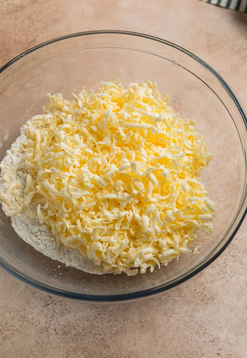 Grated butter in glass mixing bowl with flour mixture.