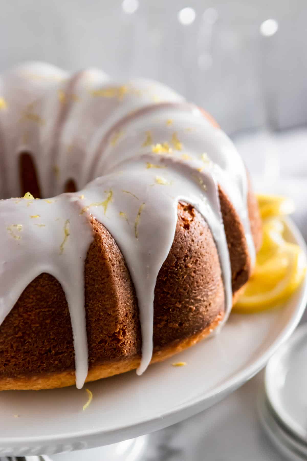 Lemon bundt cake on cake platter with lemon zest and icing.