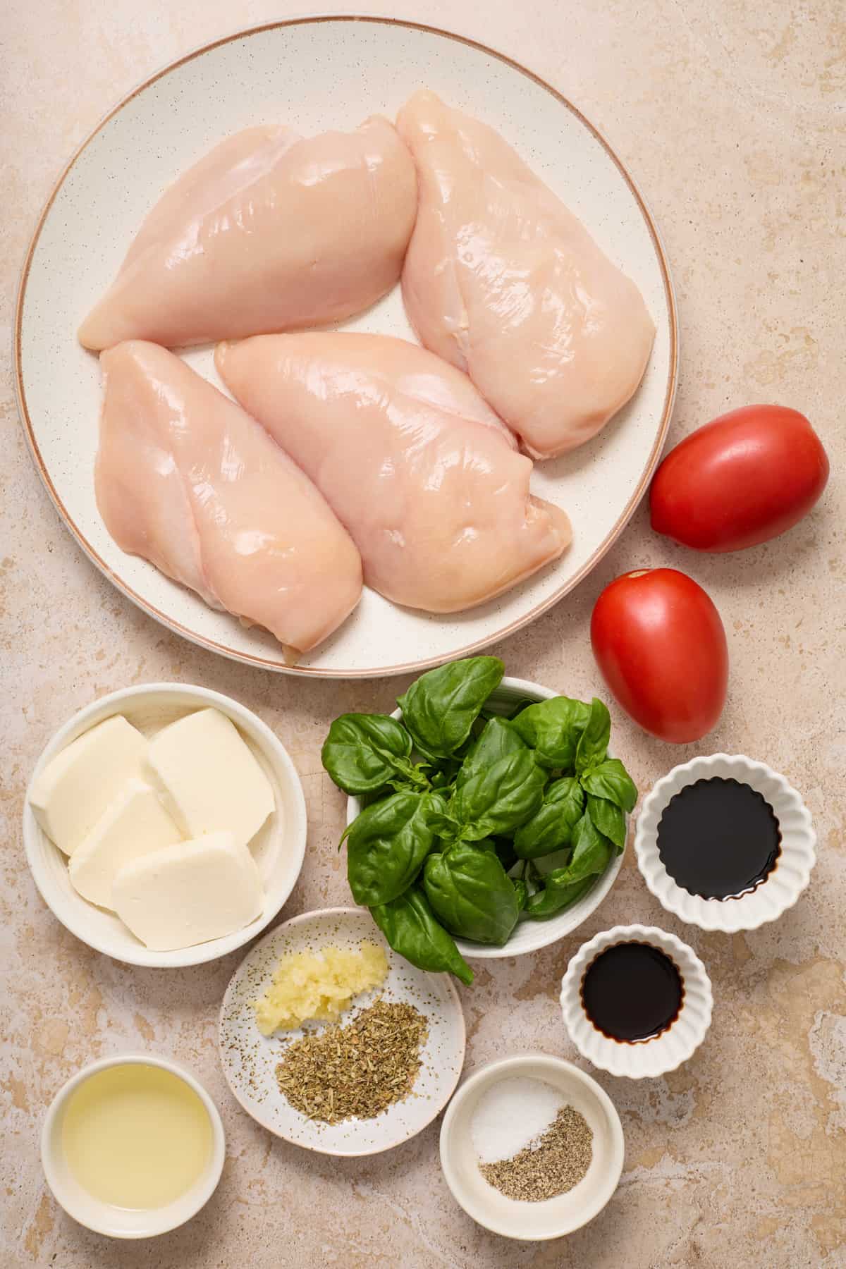 Chicken breast, mozzarella, sliced tomato, basil and other ingredients arranged on surface for recipe.
