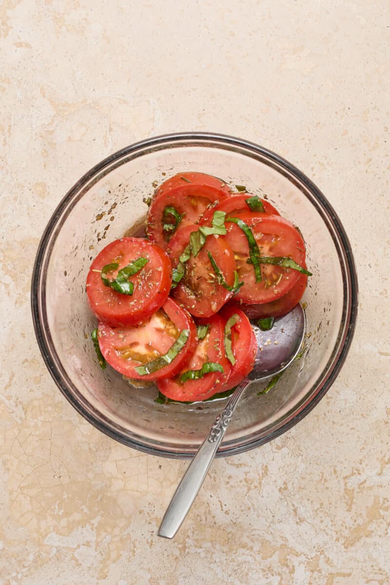Tomatoes and basil in olive oil and balsamic mixture in bowl.