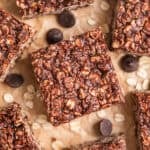 No Bake peanut butter chocolate oatmeal bars on parchment with rolled oats and chocolate chips surrounding the bars.
