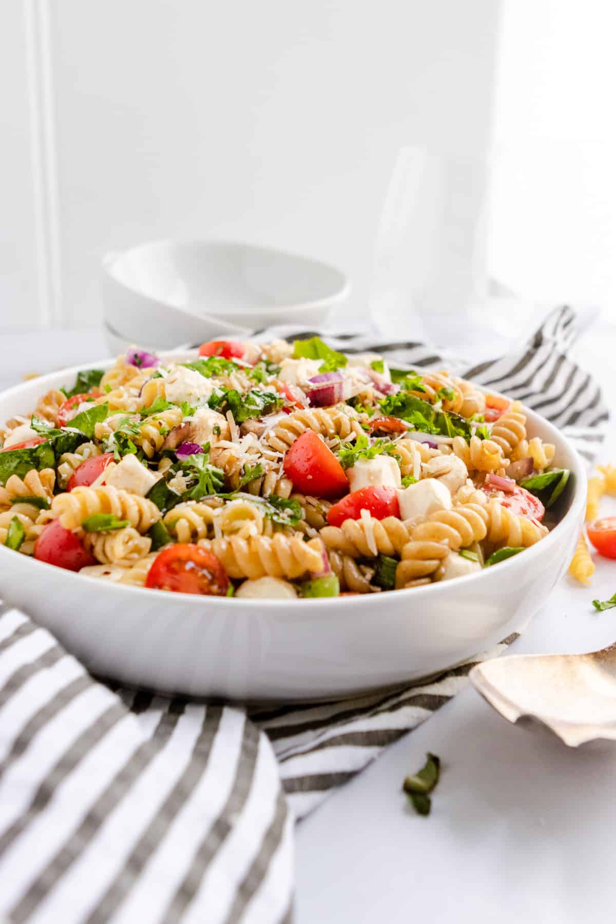 Pasta salad in white bowl with serving bowls.