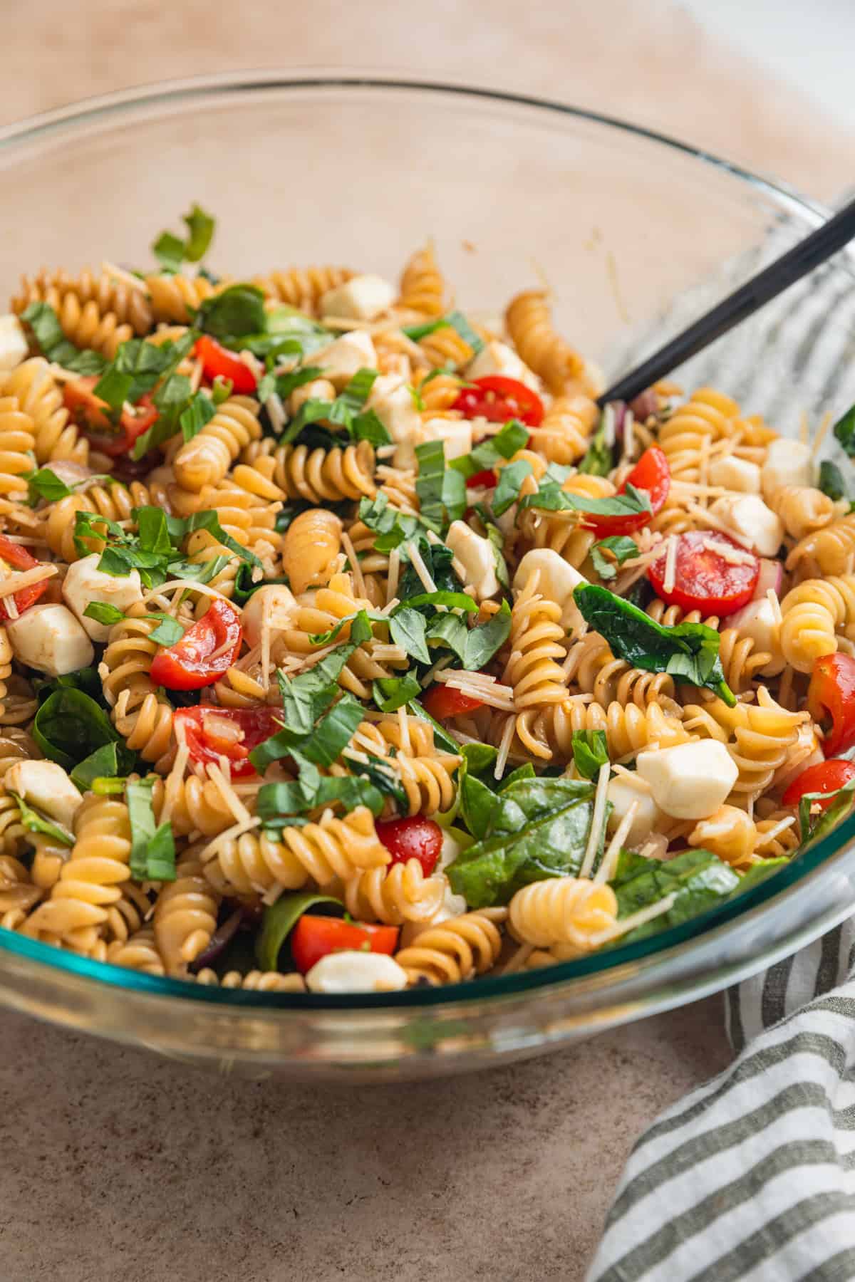 Prepped pasta salad with basil, tomatoes, mozzarella, spinach and other ingredients in bowl.
