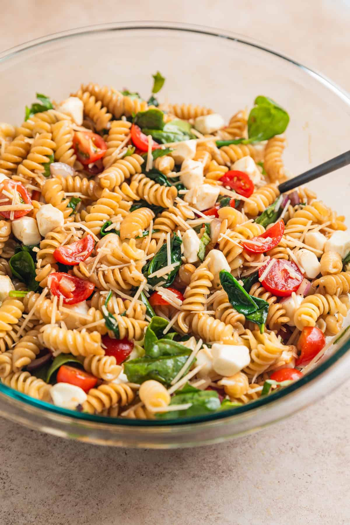 Pasta salad mixture tossed with dressing in bowl with spoon.
