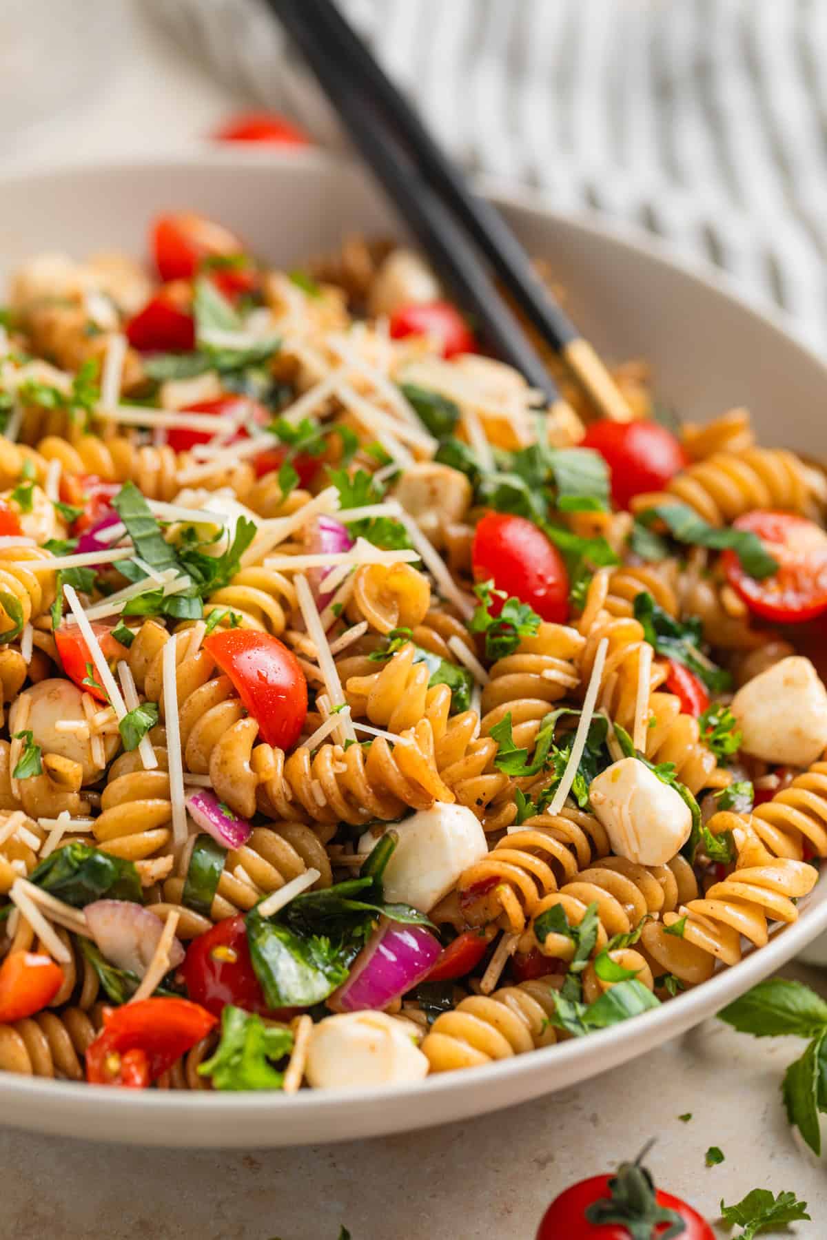 Tomato basil pasta salad with fresh mozzarella topped with chopped parsley in serving dish. 