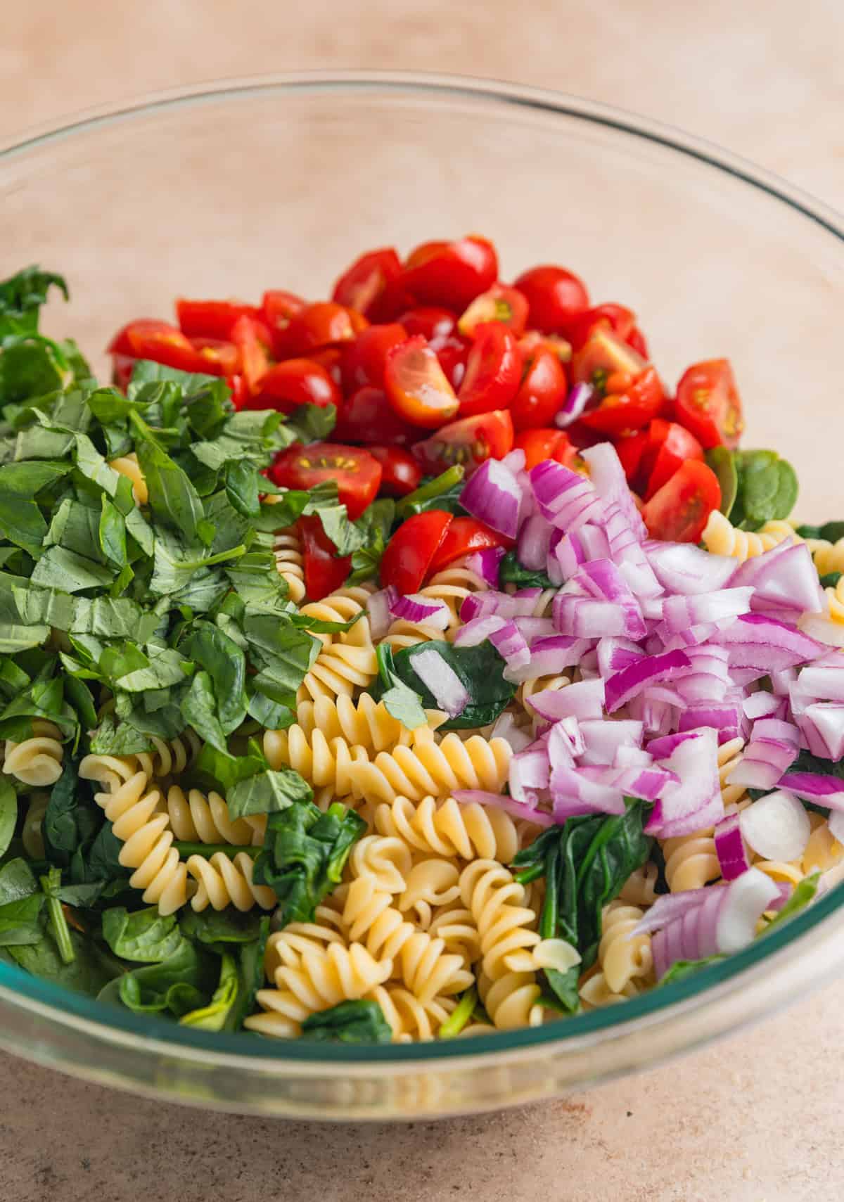 Large mixing bowl with pasta, spinach, chopped basil, tomatoes and onion.