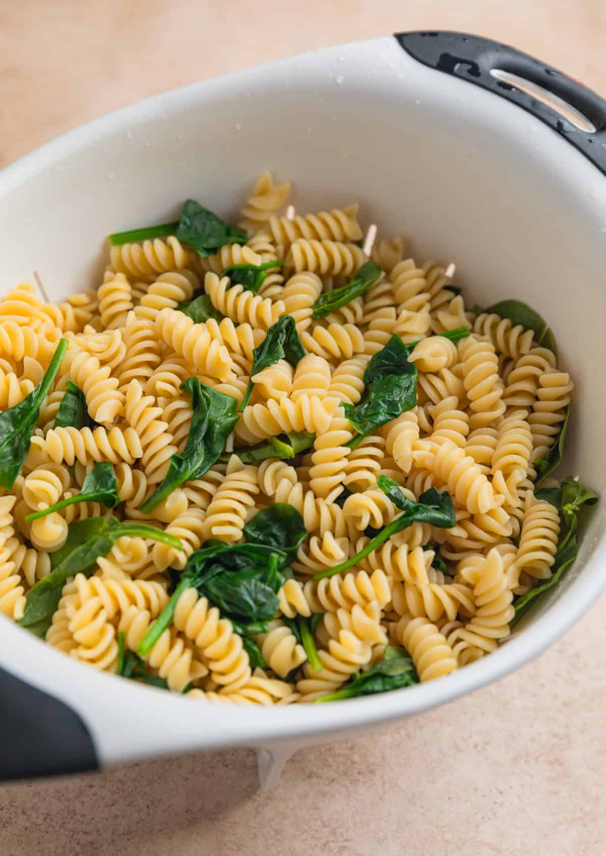 Cooked rotini pasta in colander with wilted spinach.