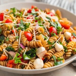 Pasta salad made with grape tomatoes, spinach, basil, mozzarella and other ingredients in serving bowl.