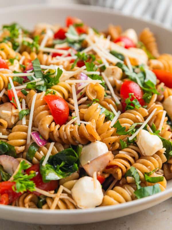 Pasta salad made with grape tomatoes, spinach, basil, mozzarella and other ingredients in serving bowl.