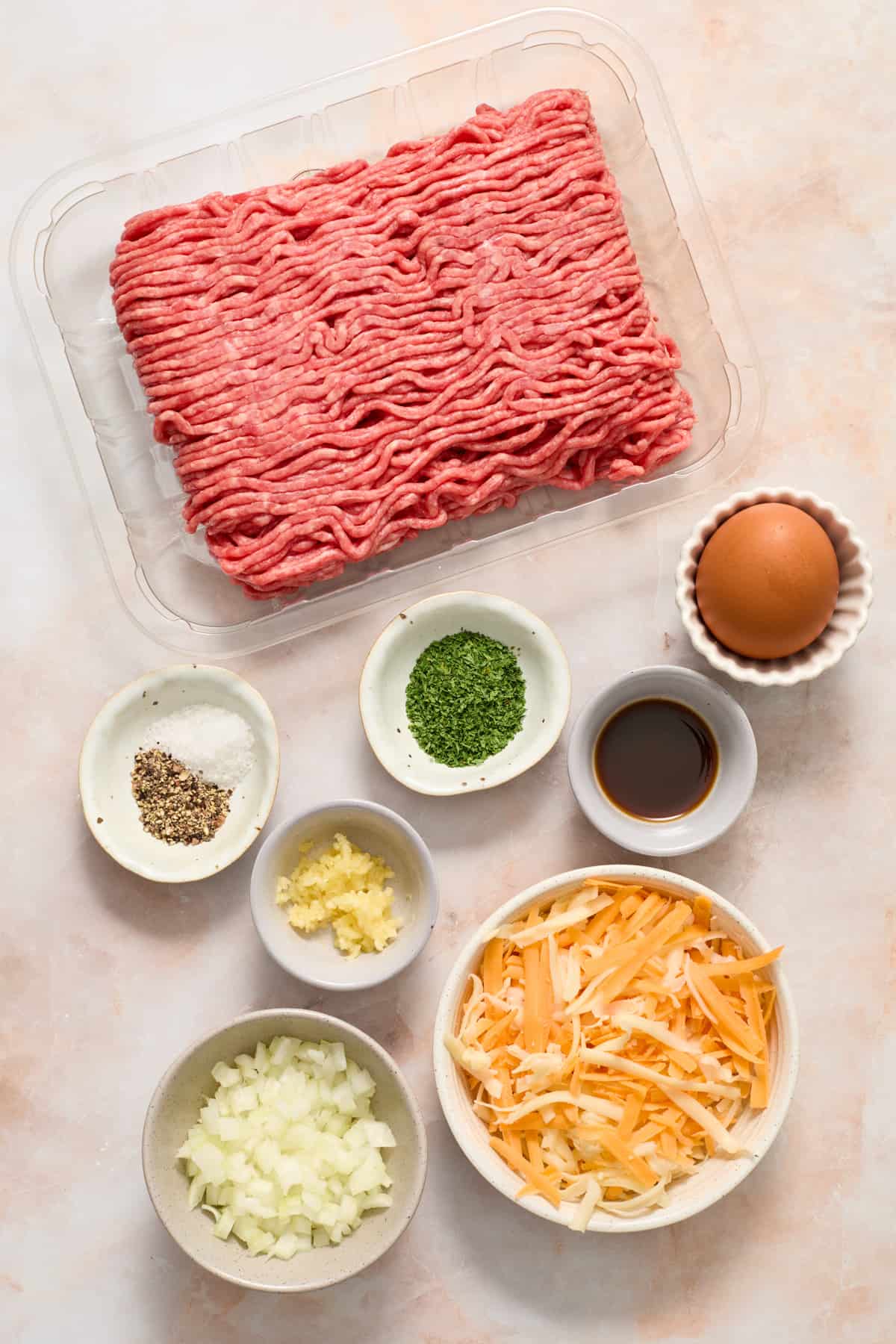 Beef, seasoning, egg, cheese, onion and other ingredients prepped for recipe.