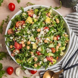 Chickpea avocado salad in bowl with arugula, feta, cucumbers, tomato and other ingredients.
