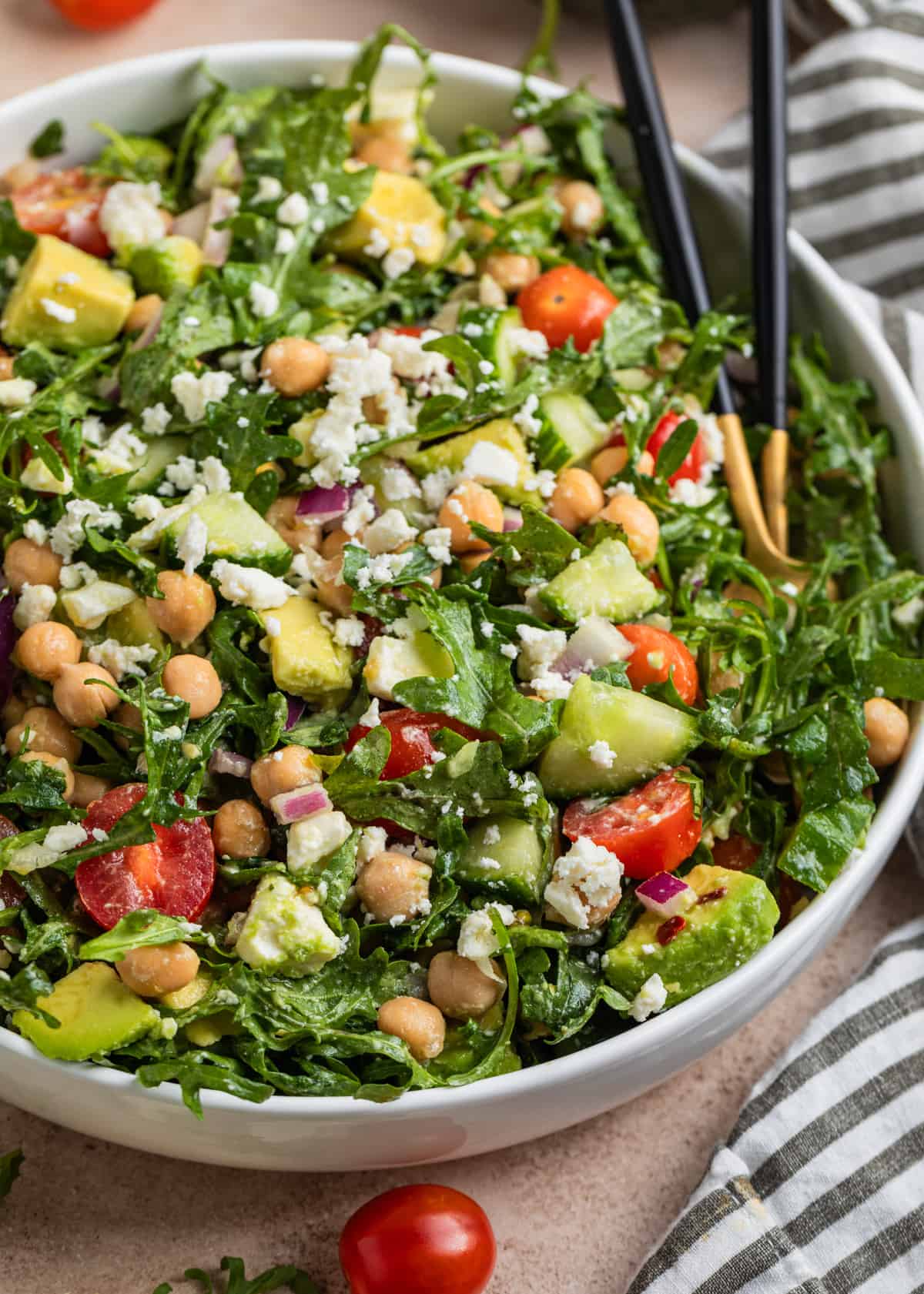 White dish with arugula, chickpea and avocado salad topped with feta cheese.