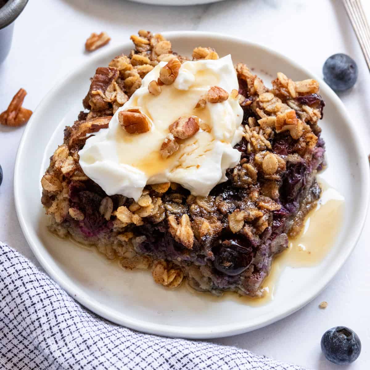 Blueberry oatmeal baked on plate with yogurt and maple syrup.